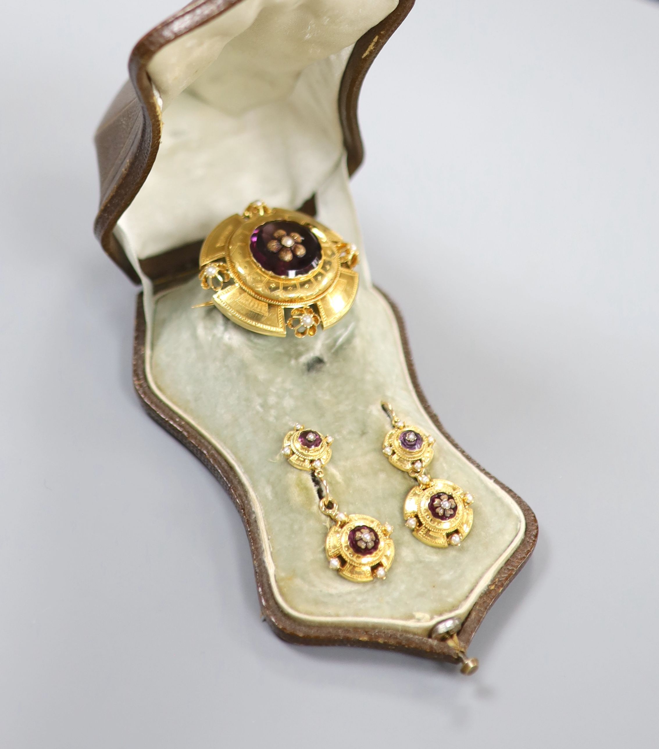 A cased continental Victorian style yellow metal, amethyst paste and seed pearl set demi parure, comprising a brooch and pair of matching earrings, brooch 35mm, earrings overall 37mm, gross weight 12.8 grams.